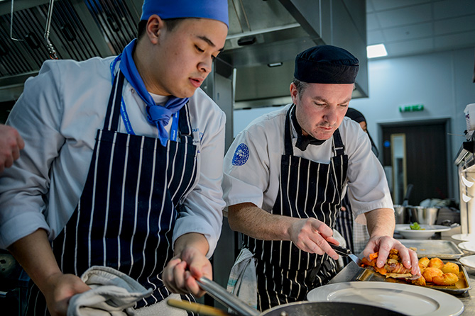 In the heat of the kitchen a catering student prepares food with the head chef